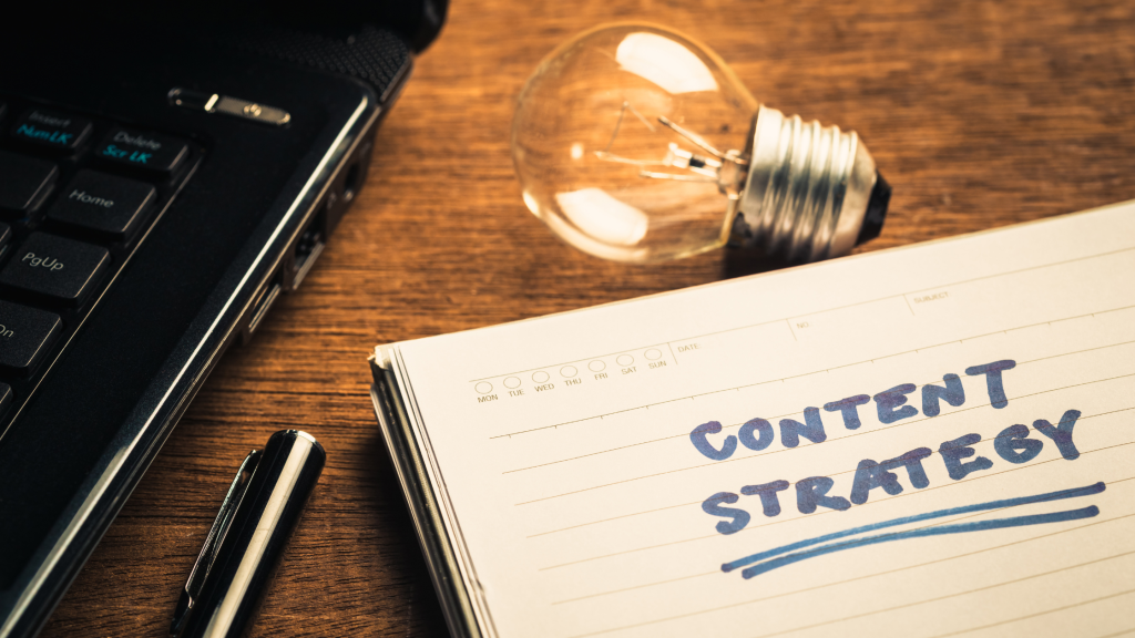 Notebook labeled “Content Strategy” beside a laptop and lightbulb on a desk.